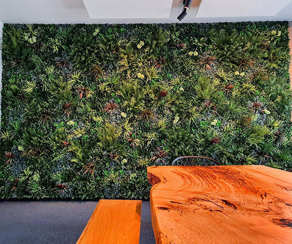 hinter einem Holztisch mit Sitzmöglichkeiten befindet sich eine Pflanzenwand aus künstlichen Pflanzen als Symbolbild für Kunstpflanzen