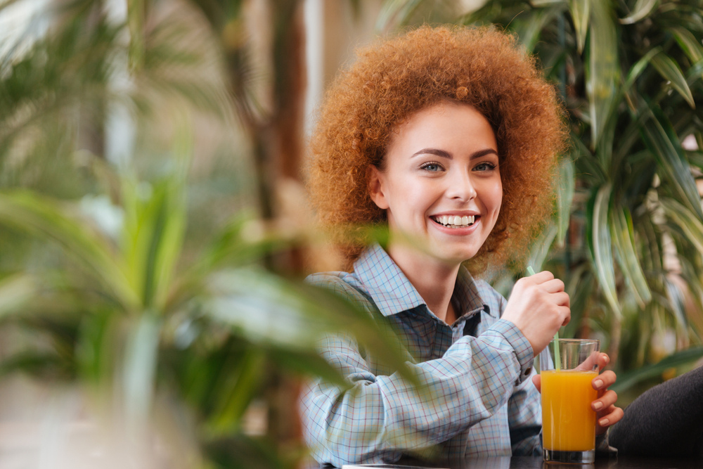 Eine Frau mit einem breiten Lächeln und einem Glas Saft in der Hand umgeben von Pflanzen